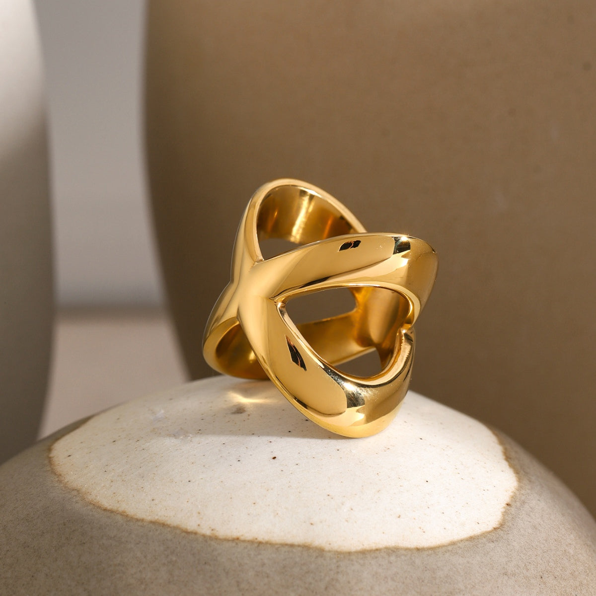 18K gold-plated crisscross ring displayed on a ceramic surface, showcasing its elegant design and shine.
