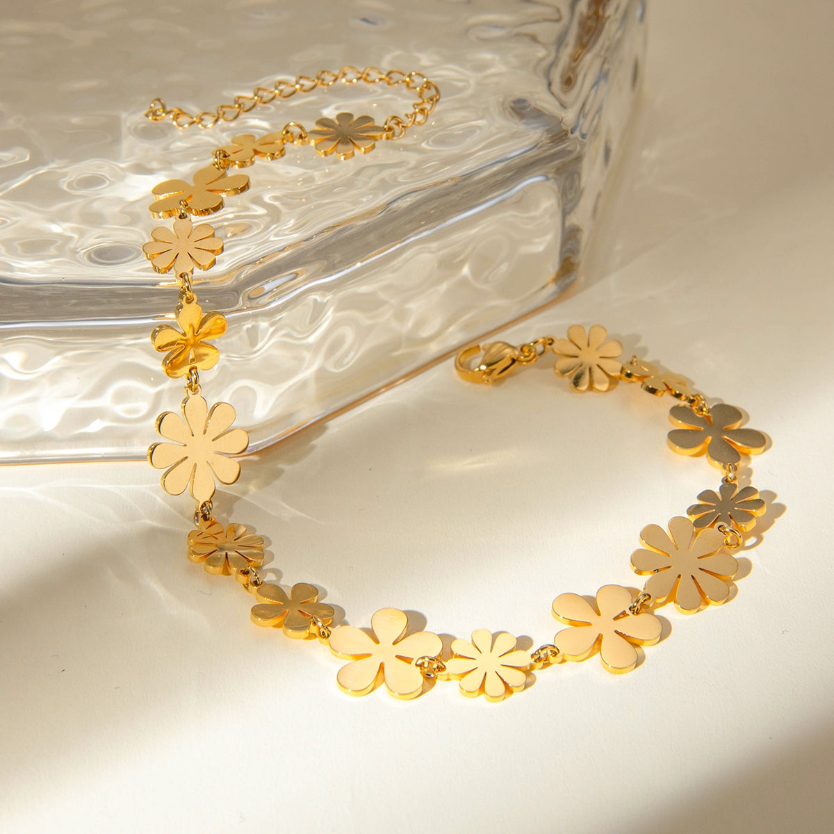 18K gold-plated flower bracelet with floral design, elegantly displayed next to a clear glass surface.