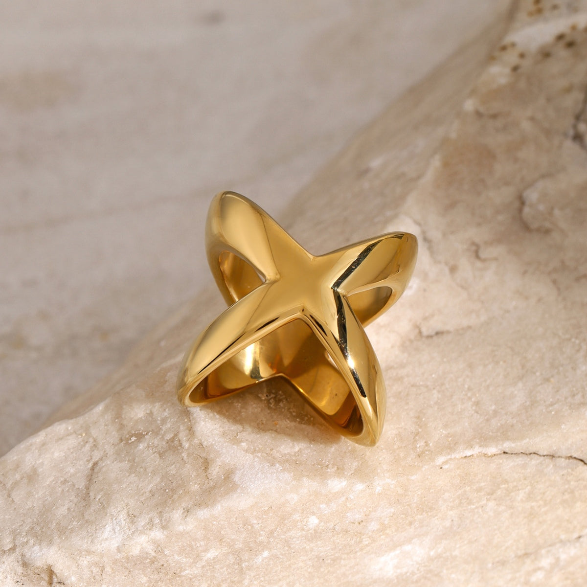 18K gold-plated crisscross ring displayed on a natural stone surface, showcasing its unique design and shine.