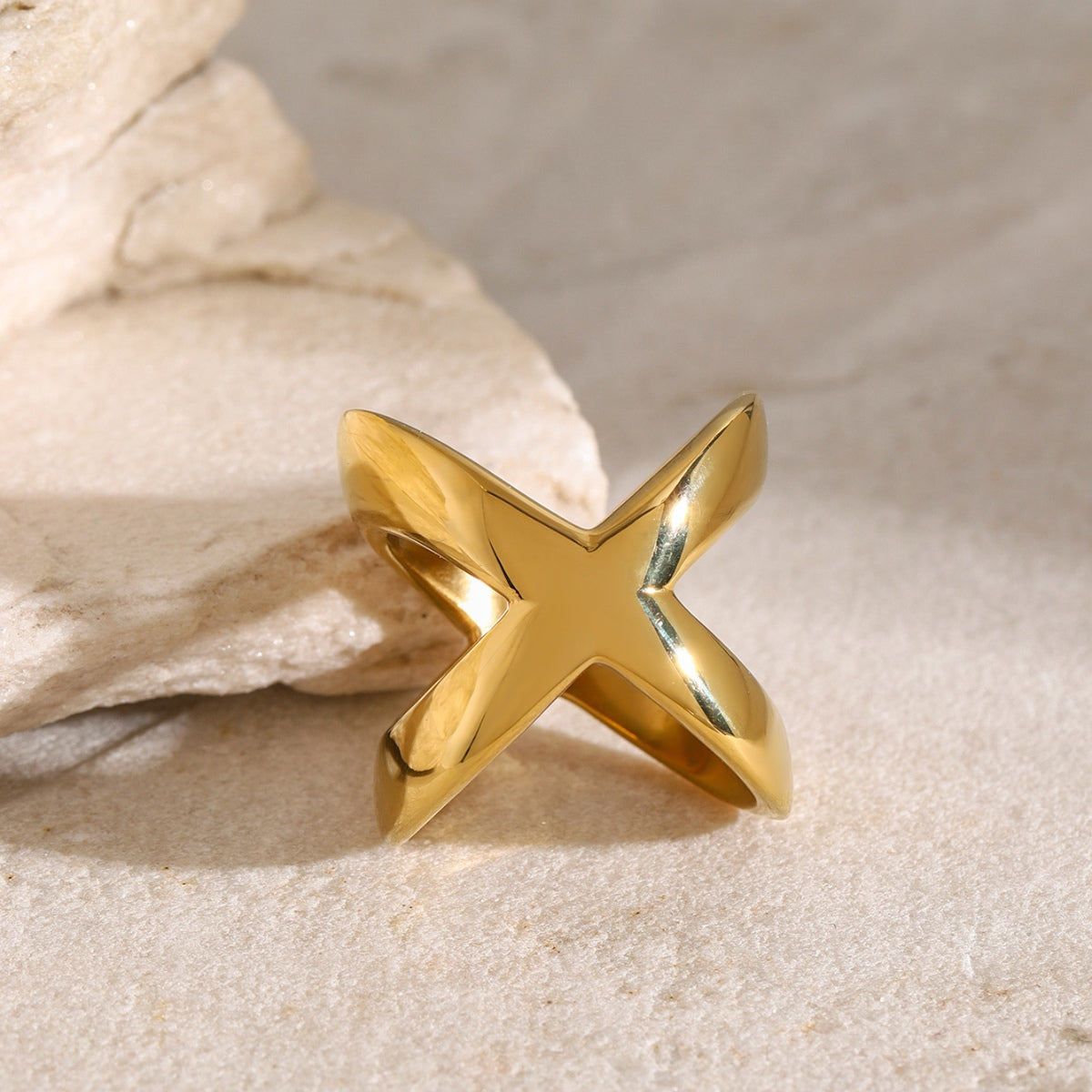 18K gold-plated crisscross ring displayed on a textured stone surface, showcasing its elegant design and shine.